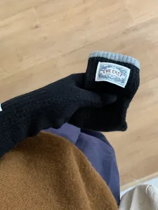 Close-up of black knitted arm warmer with grey ribbed cuff and white brand label detail