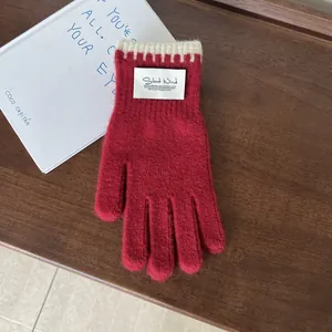 Close-up of red knit gloves with contrast striped wristband and minimalist cloth label