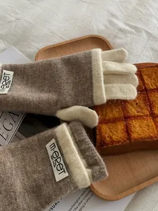 Detail of warm pumpkin orange knitted gloves with soft texture and brand tag on a wooden tray