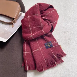 Close-up of burgundy plaid scarf texture with fringe detail and branded woven label