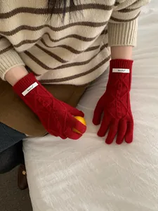 Detail showing red merino wool cable knit gloves with brand label and touchscreen fingers