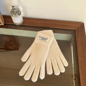 Close-up of beige knit gloves featuring a branded textile label on a wooden tray
