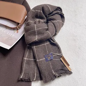 Detail of dark brown plaid cashmere-like scarf with fringe and brand label on rug