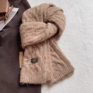 Detail of chunky cable knit wool scarf in soft camel with premium brand logo tag