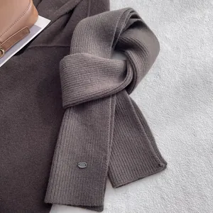 Detailaufnahme des dunkelbraunen Wollschals mit feinem Rippenstrick und Metall-Logo-Tag