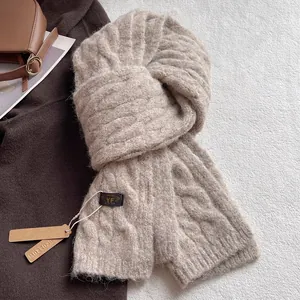 Close-up of cable knit wool scarf in oatmeal with brand label and leather tag