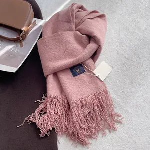 Dettaglio di sciarpa rosa in maglia spessa con lunghe nappe ed etichetta del marchio