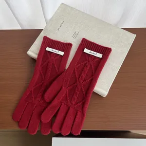 Detailed cable knit texture of dark red merino wool gloves with a small brand tag