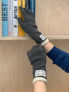 Close-up of dark grey knitted gloves with white ribbed cuffs and a decorative woven label