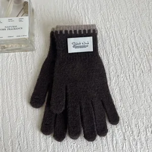 Detail of dark coffee knit gloves featuring contrast edge stitching and a white brand label