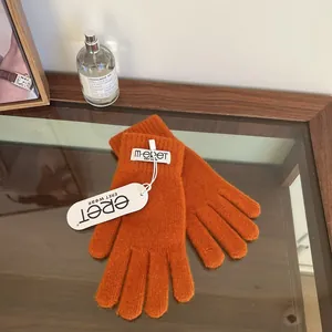 Detail of bright orange knitted gloves with woven label and elastic ribbed cuffs