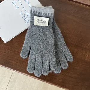 Detail of grey knitted gloves with Silent Wind woven label on dark wooden background
