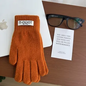 Detail of orange knitted winter gloves with a white logo tag and soft textured fabric