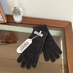 Detailed view of dark grey knit gloves with branded woven label and paper tag on desk