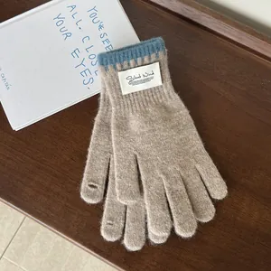 Detail of light brown knit gloves with blue ribbed cuffs and brand label on wood