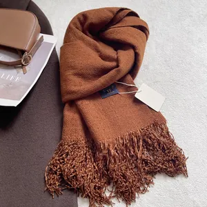 Dettaglio della sciarpa marrone caramello tipo cashmere con lunghe frange e trama morbida