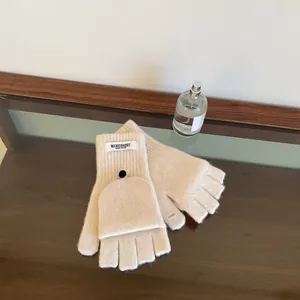 Close-up of cream wool knit convertible mittens with flap and button on wood surface