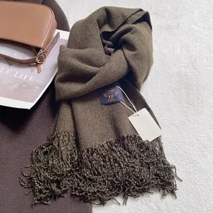 Dettaglio di sciarpa in finto cashmere marrone scuro con lunghe nappe ed etichetta di marca
