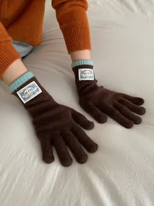 Detail of coffee brown knitted gloves with blue ribbed cuffs and decorative white label