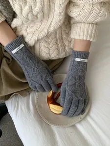 Close-up of gray cable-knit merino wool gloves with a brand label on the wrist