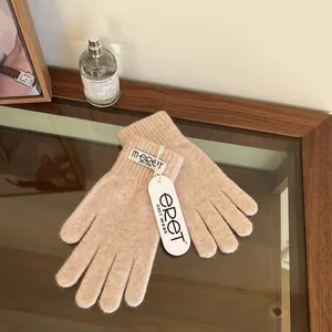 Close-up of oatmeal knit gloves with ribbed cuffs and woven brand label on a desk