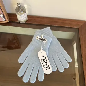 Detail of light blue knit gloves with brand tag and label on a wooden surface