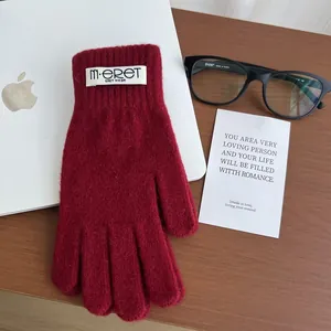 Detailed plush texture of deep red knit touchscreen gloves on a wooden desk setup