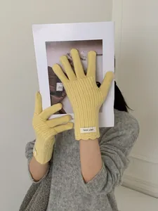 Detail of light yellow wool knit gloves featuring delicate scalloped edges and woven label