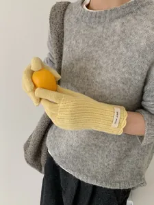 Close-up of yellow knit wool gloves with ribbed texture and ERET-WOOL logo label