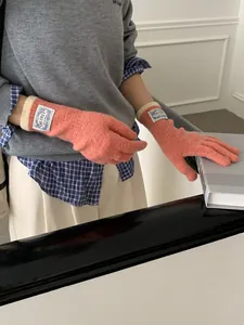 Detail of coral pink knit gloves featuring ribbed cuffs and branded fabric label