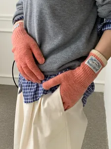 Close-up of coral pink knit gloves with rib knit cuffs and branded woven label detail