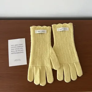 Detail of light yellow wool knit gloves featuring wavy ruffled cuffs and brand labels
