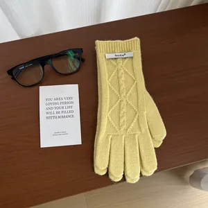 Detail of yellow merino wool knit gloves showing cable stitch texture and logo tag