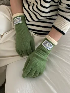 Close-up of green knit gloves with ribbed cuffs and branded fabric label detail