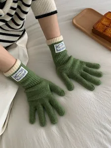 Close-up of green ribbed knit gloves with white roll-edge cuffs and logo woven label