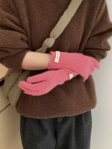 Close-up of rose pink wool knit gloves featuring vertical ribbed texture and brand label