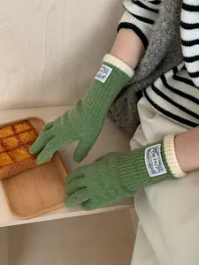 Detail of green knitted gloves with ribbed cream cuffs and elegant fabric label
