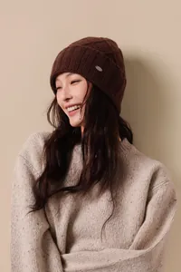 Detail of the brown wool knit beanie with a silver metal tag and ribbed texture