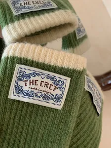 Close-up of ribbed knit texture and woven label detail on green and white gloves