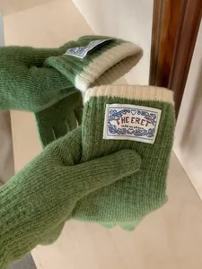 Detail view of green knit gloves with cream wrist cuffs and woven logo tag