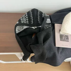 Close-up of black knitted balaclava with white geometric snowflake patterns on wood