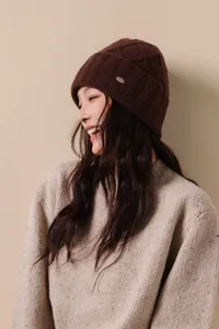 Detail of dark brown wool knit beanie featuring diamond patterns and metal brand plaque