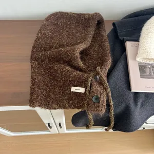 Detailopname van bruine bouclé bivakmuts van wol met knoopsluiting en merklabel detail