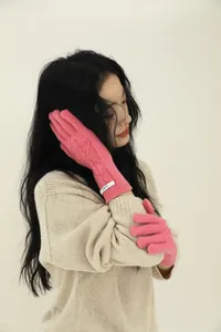 Detail of pink cable knit merino wool gloves with woven brand label and diamond patterns