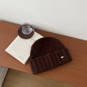 Close-up of deep brown wool knit beanie with chunky diamond pattern and metal logo