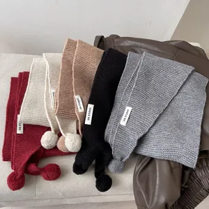 Colorful knitted scarves with pom-poms and KN STUDIO labels in diverse warm tones