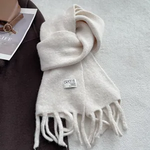 Detail of soft cream wool scarf with thick fringe and woven label on a brown coat