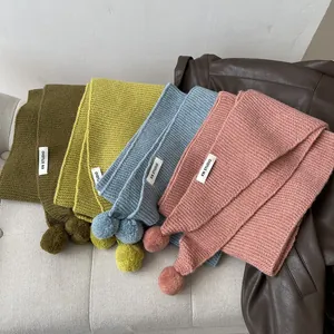 Detail of colorful knit scarves with pom-poms and brand label on a beige sofa
