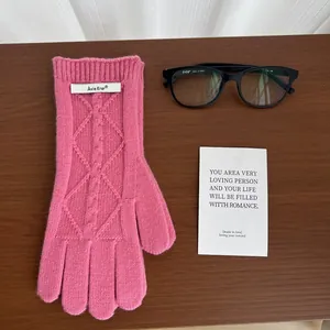 Detail of pink merino wool knit gloves with diamond patterns and branded label on wood