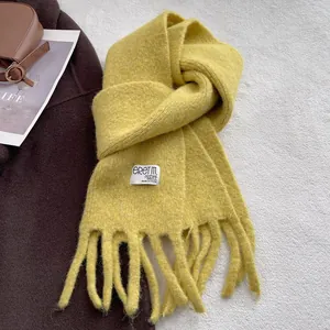 Close-up of yellow knit scarf featuring soft texture, long tassels, and a white brand label